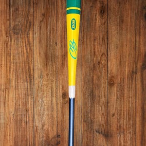 May include: A baseball bat with a pink top, green and yellow accents, and a blue handle. The bat has the text "32/29" and the initials "CB" in a teal script. The bat is set against a wooden background.