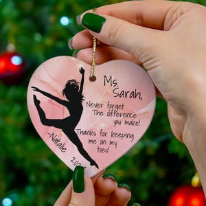 Puede incluir: Adorno de cerámica en forma de corazón rosa con una silueta de una bailarina y el texto "Ms. Sarah, Nunca olvides La diferencia que haces! Gracias por mantenerme en mis dedos de los pies! -Natalie 2021"
