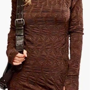 May include: A long-sleeved, brown dress with a textured, geometric pattern. The dress has a crew neck and fitted sleeves. A black leather shoulder bag with a silver buckle is visible. The dress is knee-length and has a slit on the side.