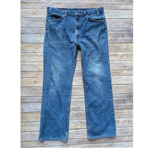 May include: A pair of medium-wash blue denim jeans featuring a classic five-pocket design, a button and zip fly closure, belt loops at the waistband, and a straight-leg cut with subtle fading on the front of the thighs and knees.