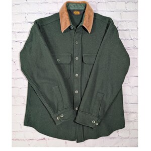 May include: A dark green long-sleeve button-up shirt featuring a tan corduroy collar, two chest pockets with buttoned flaps, and buttoned cuffs. The shirt has a central button placket and a dark green inner lining visible at the collar area.