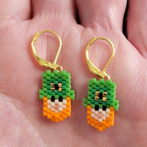Könnte beinhalten: Ein Paar goldene Creolen mit grünen, orangefarbenen und weißen Perlen-Leprechaun-Anhängern.