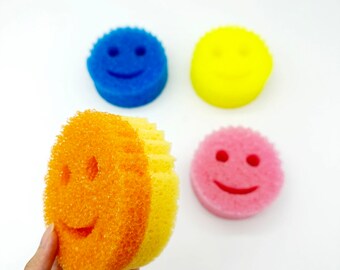 May include: Four colorful smiley face sponges. The sponges are yellow, blue, pink, and orange. The orange sponge is a two-tone sponge with a yellow stripe.