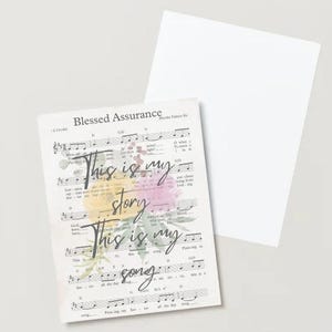 May include: A sheet music print featuring the hymn "Blessed Assurance" with the words "This is my story, This is my song." Floral watercolour accents in yellow, pink, and green. A blank white card is next to it.