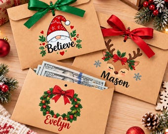 Puede incluir: Tres sobres de papel kraft marrón con diseños navideños. Uno presenta un gnomo y la palabra Believe con una cinta verde. Otro muestra un reno y el nombre Mason con una cinta roja. El tercero exhibe una corona y el nombre Evelyn.