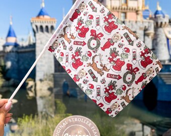 May include: A white stroller flag with a repeating pattern of red and green cartoon characters, gifts, and wreaths. The flag is held up in front of a castle. The text "STANK" and "SUK" are visible on the flag.