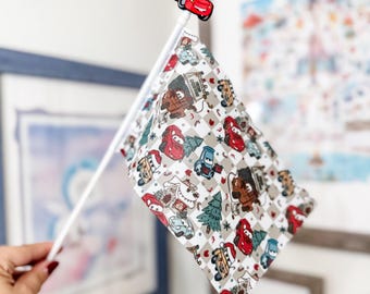 May include: A white flag with a red car topper. The flag features a pattern of cartoon cars, Christmas trees, and other holiday-themed elements on a gray and white checkered background. The flag is held up by a white pole.