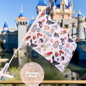 May include: A white stroller flag with a repeating pattern of cartoon characters and icons. The flag is held by a white pole and clip. The text "METROFLOOD" is visible on the flag. The flag is in front of a castle.