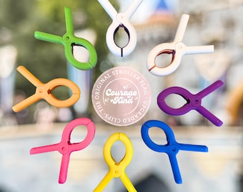 May include: A collection of colorful stroller flag clips in green, white, orange, purple, pink, yellow, and blue. The clips are arranged in a circular pattern around a central emblem that reads "Courage + Kind".