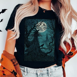 May include: A black t-shirt with a graphic print of a spooky tree with a full moon and a crow. The tree has a face and is silhouetted against the moon.