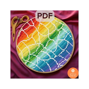 Peut inclure: Un motif de point de croix coloré dans un cercle en bois, avec un motif arc-en-ciel et des lignes de grille blanches. L'image comprend des ciseaux en bois et le texte "PDF". Le logo Stitch Dream est visible.
