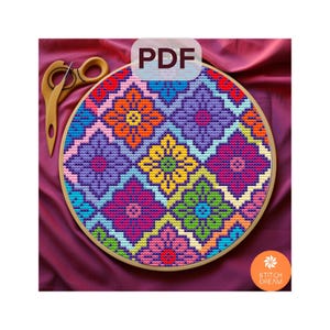 Op de afbeelding: Een kleurrijk kruissteekpatroon in een houten borduurring. Het ontwerp toont geometrische bloemvormen in tinten paars, oranje, geel, groen en roze. Het woord "PDF" is zichtbaar. Een houten schaar is links.