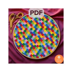 May include: A colorful cross-stitch pattern of a geometric design with a variety of colors, including red, orange, yellow, green, blue, purple, and pink. The pattern is stitched on a white fabric and is framed in a wooden hoop. The image includes the text "PDF".