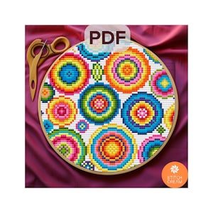 Puede incluir: Un patrón de punto de cruz colorido con círculos concéntricos de varios tamaños y tonos vibrantes de azul, verde, amarillo, naranja y rosa. El diseño está dentro de un bastidor de bordado de madera. La palabra "PDF" es visible en la parte superior central.