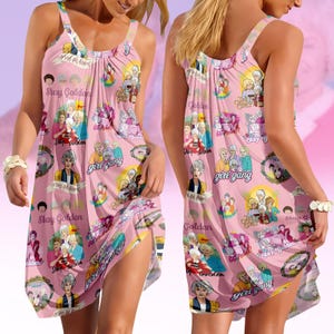 Puede incluir: Vestido rosa pálido sin mangas con un patrón repetido de ilustraciones y texto. El texto incluye "Stay Golden" y "Girl Gang". El vestido tiene un escote redondo y una silueta fluida.