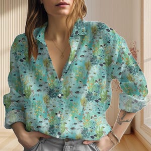 Può includere: Camicia azzurra con bottoni e motivo acquatico. La camicia presenta un design di pesci, alghe e coralli. Ha un colletto classico e una chiusura con bottoni. Le maniche lunghe sono visibili.