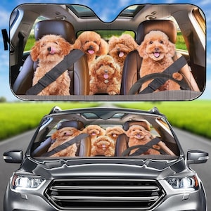 Könnte beinhalten: Ein Autosonnenschutz mit einem lustigen Design von braunen Hunden in einem Auto, die alle einen Sicherheitsgurt tragen. Die Hunde scheinen zu fahren und auf den Vordersitzen des Autos zu sitzen. Der Sonnenschutz ist für die Windschutzscheibe eines Autos konzipiert.