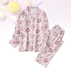 Può includere: Set pigiama rosa con un motivo ripetuto di dolci, tazze da tè e cuori su sfondo a scacchi. La parte superiore a maniche lunghe ha una chiusura con bottoni e un colletto a revers. I pantaloni abbinati hanno una vita elasticizzata.