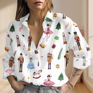 Könnte beinhalten: Weißes Button-Down-Hemd mit einem sich wiederholenden Muster von weihnachtlichen Illustrationen. Das Design umfasst Nussknacker, Ballerinas, Weihnachtsbäume, Uhren und Geschenkboxen in verschiedenen Farben. Das langärmlige Hemd hat einen Kragen.