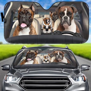 May include: Car sunshade with a comical design of Boxer dogs inside a car. The dogs are shown in the front seats, with a puppy in a car seat. The sunshade is black, set against a blue sky.