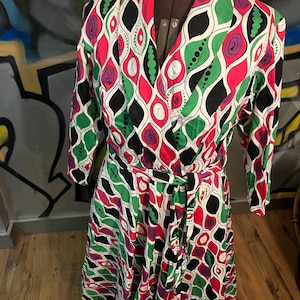 May include: A vintage wrap dress with a colorful abstract print featuring green, pink, black, and white. The dress has a long sleeve and a tie at the waist.