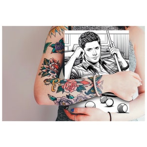Pode incluir: Um braço com tatuagens florais e náuticas coloridas, segurando uma ilustração em preto e branco de um homem com um taco de bilhar. A ilustração também inclui bolas de bilhar.