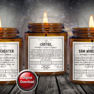 May include: Three lit amber glass jar candles with white labels. The labels read "Dean Winchester", "Castiel", and "Sam Winchester". Each candle has a different scent description. The candles are labeled "Natural Essence Candle".