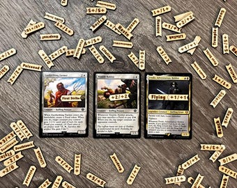 May include: Three Magic: The Gathering cards with wooden tokens. The cards feature characters and abilities like "First Strike" and "Flying." Wooden tokens with game effects like "+1/+1" and "Lifelink" are scattered around the cards.