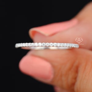 May include: A thin silver band with a row of small, clear diamonds set in a pave setting.