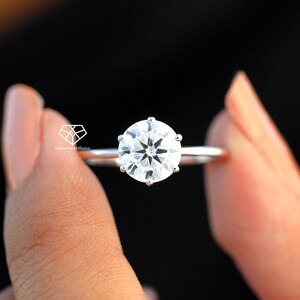 Pode incluir: Um anel de noivado de prata com um grande diamante redondo e claro.