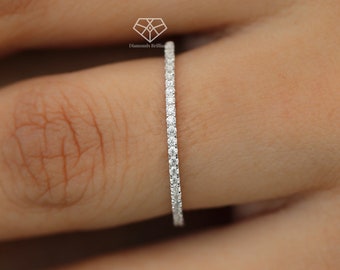 May include: A thin, white gold wedding band with a row of small, round diamonds set in a pave setting.