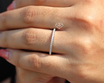 Könnte beinhalten: Ein dünner, silberner Ring mit einer Reihe kleiner, klarer Diamanten, die in Pavé-Fassung gefasst sind. Der Ring wird an einem Finger getragen.