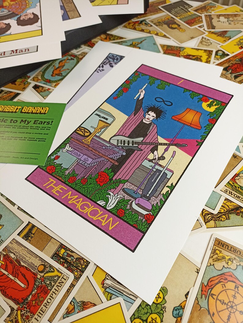 May include: A tarot card print titled THE MAGICIAN featuring a figure with dark hair holding a drumstick and microphone, wearing a purple robe. The scene includes a guitar, a floor lamp, a vacuum cleaner, and a golden chalice on a table.