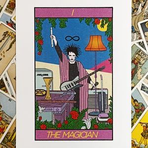 May include: A rectangular art print featuring a tarot card illustration titled THE MAGICIAN. The image depicts a person with dark hair holding a drumstick and microphone, wearing a pink robe, standing behind a table with a guitar and objects.