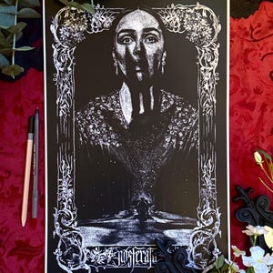 May include: Black and white art print featuring a woman's portrait within an ornate frame. The artwork has a gothic aesthetic, with intricate floral and scroll details. The word "Nosferatu" is visible at the bottom of the print.