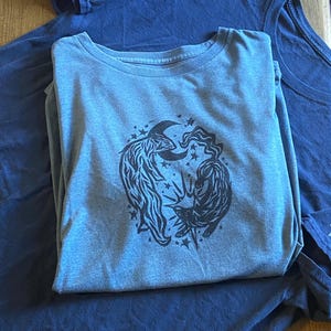 May include: A blue t-shirt with a black and white graphic print of two animals with a crescent moon and stars.