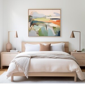 K&ouml;nnte beinhalten: Ein Bett mit einem hellen Holzrahmen, einer wei&szlig;en Bettdecke und einer beigefarbenen Wolldecke. Das Bett hat zwei wei&szlig;e Kissen und ein braunes Kissen. &Uuml;ber dem Bett h&auml;ngt ein gerahmtes abstraktes Landschaftsbild.