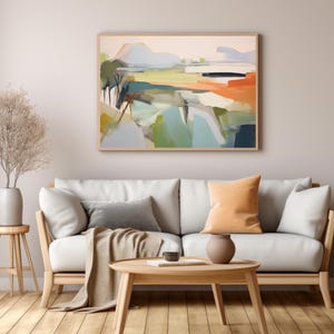 K&ouml;nnte beinhalten: Ein wei&szlig;es Sofa mit zwei Kissen, einer Wolldecke und einem Holz-Couchtisch vor einer hellgrauen Wand mit einem gerahmten abstrakten Landschaftsbild &uuml;ber dem Sofa.