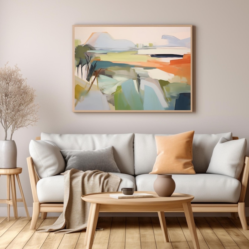 K&ouml;nnte beinhalten: Ein wei&szlig;es Sofa mit zwei Kissen, einer Wolldecke und einem Holz-Couchtisch vor einer hellgrauen Wand mit einem gerahmten abstrakten Landschaftsbild &uuml;ber dem Sofa.