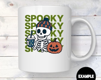 May include: White ceramic mug featuring a cartoon skeleton wearing a knit cap, holding a beverage, and next to a jack-o'-lantern. The word "SPOOKY" is printed in green multiple times. A black circle with the word "EXAMPLE" is at the bottom.