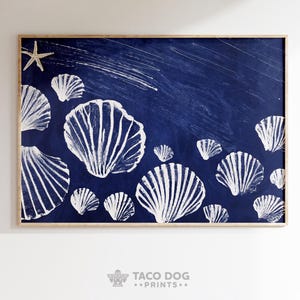 Pode incluir: Uma impressão emoldurada com ilustrações de conchas brancas sobre um fundo azul escuro. Uma estrela do mar e algumas listras brancas também estão presentes. A obra de arte tem um tema náutico e é adequada para decoração costeira.