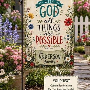 May include: A rectangular garden flag featuring a cream-colored background with a green checkered border. The text reads WITH GOD all THINGS are POSSIBLE Matthew 19:26. Below, a green banner displays The ANDERSON Family. Colorful wildflowers surround the text.