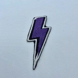Może przedstawiać: Naszywka z błyskawicą w kolorze fioletowym z białym obramowaniem, do prasowania.