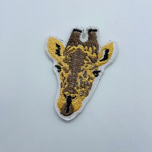 May include: An embroidered patch of a giraffe's head, featuring brown and yellow stitching. The giraffe has a long neck and large ears.