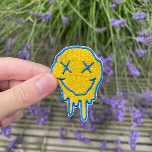 May include: Yellow smiley face iron-on patch with blue outline and dripping detail. The smiley face has an X for eyes.