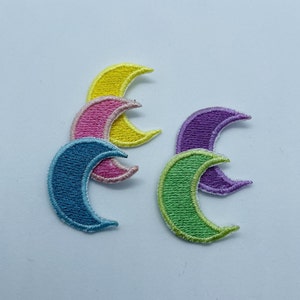 Op de afbeelding: Vier halve maanvormige stoffen patches in verschillende kleuren: geel, roze, blauw en groen. De patches zijn gestikt met wit garen.