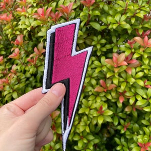 May include: Pink lightning bolt shaped iron-on patch with white and black outlines.