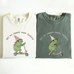 May include: Two t-shirts, ivory and moss green, with a frog graphic riding a scooter. The ivory shirt says "Off to commit aunt foolery" and the moss green shirt says "Off to commit uncle foolery". The frog wears a hat.