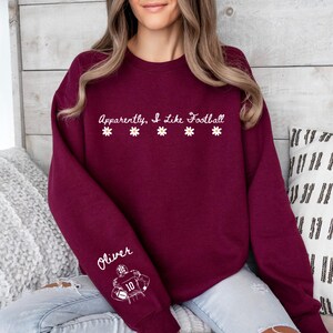 Peut inclure: Sweat-shirt bordeaux avec l'inscription "Apparently, I Like Football" et des marguerites. La manche porte le nom "Oliver" et un graphisme de joueur de football. Le sweat-shirt est de couleur bordeaux unie.