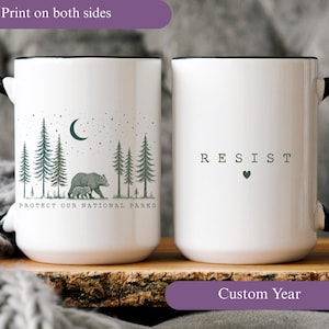 May include: White ceramic mug with a black handle and rim. One side features a forest scene with a bear and cub, the text "PROTECT OUR NATIONAL PARKS". The other side has the word "RESIST" with a heart symbol.